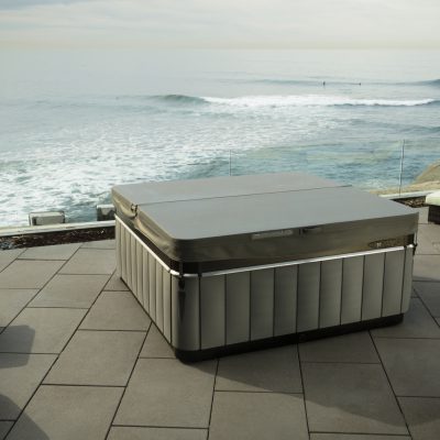Caldera Utopia spa on stone patio with cover on and sea view