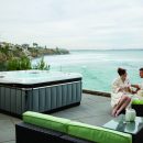 Couple sat beside Caldera Utopia series hot tub with sea view