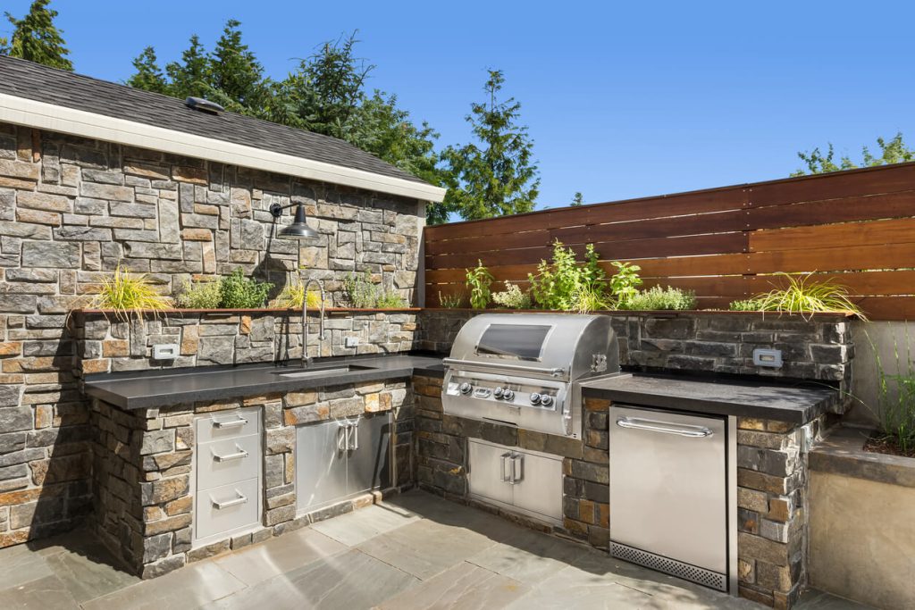 Stylish stone outdoor kitchen with built-in grill, sink, and stainless steel appliances.